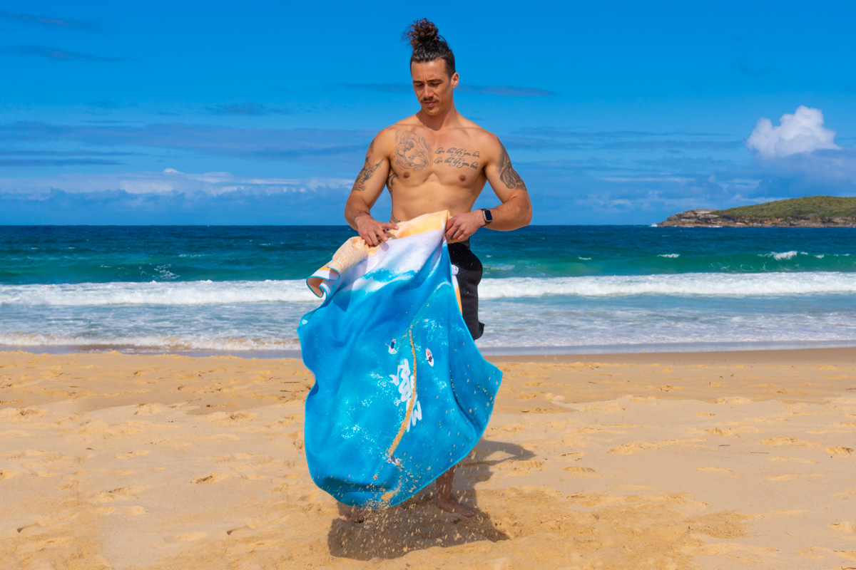 Man holding a Wandrful sand-free beach towel, at the beach, flicking of sand.